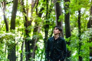 Handsome man standing alone while looking around. Beautiful dramatic deep forest greenery. photo