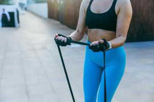 A woman is trains with a resistance band while standing outside photo