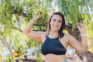 A woman is posing in front of a tree with her arms raised, photo with copy space