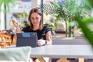 A woman is sitting at a table working with a tablet, she has a happy and relaxed expression photo