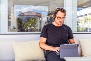 A man is sitting on a couch with a tablet in front of him, he is working in a coworking space photo