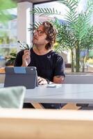 A man is sitting at a table with a tablet and a pen and has a thoughtful expression photo
