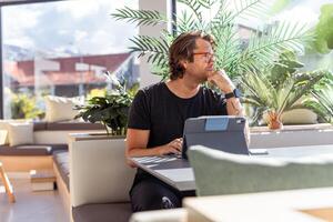 A hipster businessman is sitting at a table with a tablet and has a thoughtful expression photo