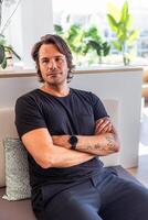 A man with a watch on his wrist sits on a couch with his arms crossed, photo with copy space
