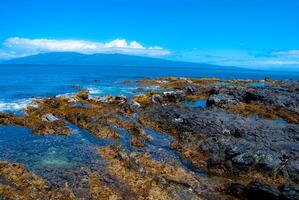 Rocky Tidepools on the Coast of Maui, Hawaii with an Island and Clouds in the Distance photo