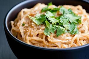 bowl of spicy Sichuan noodles topped with fresh herbs and sesame photo