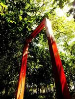 low angle view. Red archway in a forest with sunlight shining through it. The archway is surrounded by trees and bushes, creating a serene and peaceful atmosphere photo
