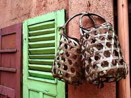 Two baskets made from woven bamboo, hanging on the pink wall. There is a green wooden window photo