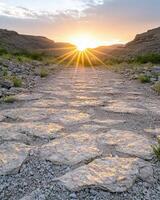 Sun rays bursting through a mountain pass illuminating a stone path photo