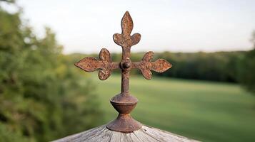 Rusty cross on a wooden surface with a blurred background of green field and trees photo