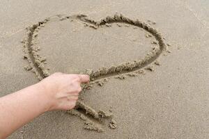 Handwritten heart shape on beach sand with space for writing a message. photo