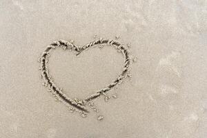 Symbol of heart written by hand on sand of beach with copy space photo