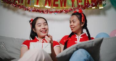 Cheerful young woman is holding a red envelope and chatting happily with her mother in the cozy living room. Asian family celebration Lunar New Year together photo