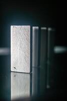 Close up of a row of white dominoes standing on a reflective surface, with the focus on the first domino in the foreground photo