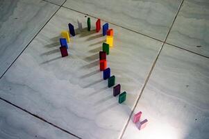 The Colorful dominoes arranged in a question mark shape on a tiled floor, casting shadows. This creative setup is visually striking and thought provoking photo
