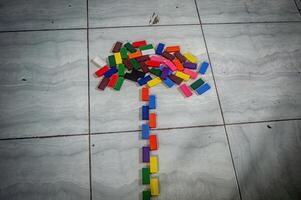 Colorful dominoes arranged like a tree on a tiled floor. A vibrant display of red, blue, green, yellow, and other hues creating a playful design photo