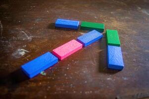 Colorful wooden blocks arranged in the shape of an arrow on a wooden surface. The blocks are blue, pink, and green, creating an interesting visual contrast photo