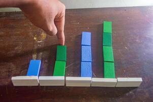 A hand points to a colorful bar chart made of wooden blocks on a wooden surface, illustrating data comparison in a simple and engaging way photo