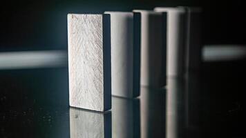 The Close up of a row of white dominoes standing on a reflective surface, with the focus on the first domino in the foreground photo