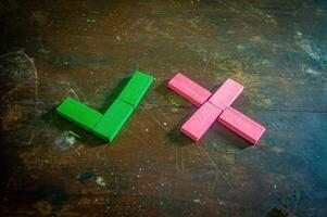 Wooden blocks arranged in green check mark and red cross shapes on a rustic wooden surface, symbolizing correct and incorrect choices photo