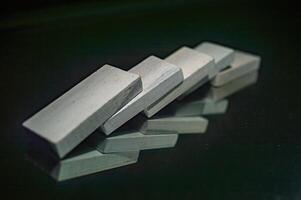 A close up image of five white rectangular blocks arranged in a domino effect on a reflective surface, creating an interesting visual pattern with their reflections photo