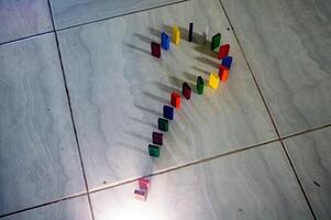 Colorful dominoes arranged in a question mark shape on a tiled floor, casting shadows. The arrangement and lighting create an intriguing visual effect photo