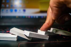 A close up of a finger pushing over a row of white dominoes on a laptop keyboard, symbolizing the domino effect in a digital context photo
