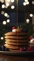Pouring maple syrup onto stack of pancakes with berries, closeup photo