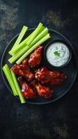 Barbecue chicken wings with celery and sauce as top view on a modern design plate photo
