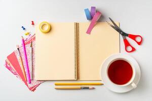 Creative workspace with stationery, colorful papers, scissors, and a cup of tea on a bright surface photo