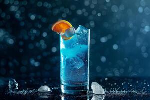 Blue cocktail with ice cubes and orange slice on a wet black surface is sparkling on blue bokeh background photo