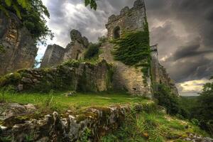 Ruins of ancient castle overgrown with ivy under stormy sky photo