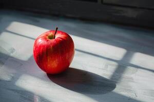 One red apple casting shadow on white table in sunbeam photo