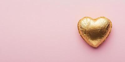 Heart shaped gold foil wrapped chocolate on pink background for festive or romantic occasions photo