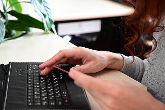 A moment captured just before a financial decision, with a hand moving toward a credit card, placed on a desk alongside a keyboard, indicating a transaction is in progress photo