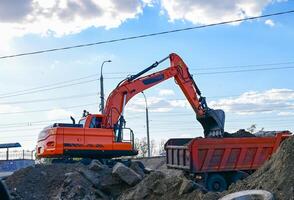 On a beautiful sunny morning Excavator during earthmoving at open pit on blue sky background. Construction machinery and earth-moving heavy equipment for excavation, loading, lifting photo