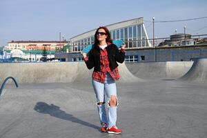 The photograph captures a casual yet stylish look of a person with a skateboard, set against a plain gray wall, highlighting modern, youth-oriented style photo