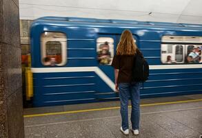 The image captures the atmosphere of a subway station, with a person sitting on a bench and a train swiftly moving along the tracks photo