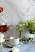 The image presents an elegant and serene scene, featuring a white teacup and fresh flowers in a calming, soft-lit setting. photo