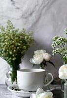 A still life composition with a white teacup, saucer, and various floral arrangements against a textured, neutral background photo