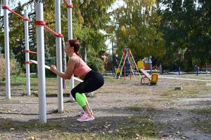 The image showcases a woman with her hands on her hips, a pose indicating strength and confidence, as she stands in a park during the fall. photo