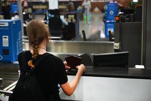 A young person with shoulder-length hair, wearing a brown shirt and blue jeans, sits on a bench in a subway station behind a granite pillar. photo