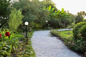Landscape design On a wonderful day in green garden, panoramic view of nice landscaped yard of residential house. Paving path, plants and vintage lantern in home backyard photo