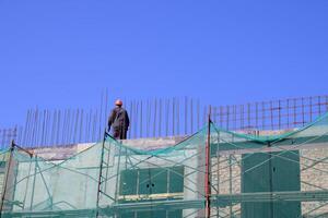 The image portrays a building under construction, with a worker visible on the upper level, highlighting the work in progress photo