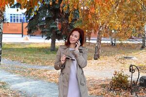 The image portrays a woman in a light-colored outfit, with a scarf and a background full of autumn colors, emphasizing the season's beauty photo
