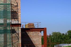 construction worker is visible at a building site, which includes brickwork, scaffolding, and steel beams under a clear blue sky photo