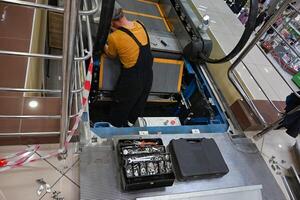 Man repairs escalator on a wonderful day, steps inside, standing with her back near the step, tools are. photo