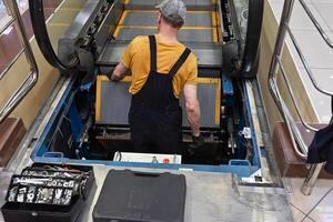 Man repairs escalator, steps inside, back near the step, tools are. photo