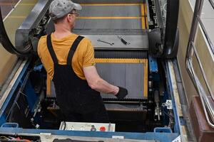Man repairs escalator On a wonderful day with a positive attitude, steps inside, standing with her back near the step, tools are. photo
