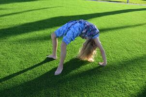 Blonde girl dancing, jumping, doing acrobatics and posing, in a city park on green grass near a lake on a sunny day photo